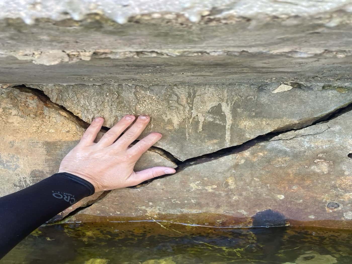 Diver's hand next to a crack in a concrete seawall during an inspection