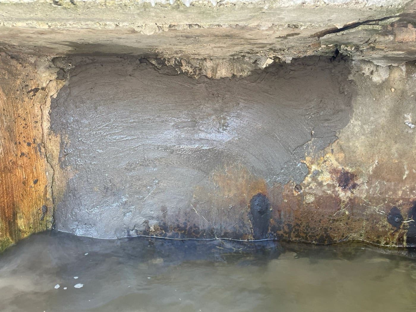 Seawall with a large void where the concrete has eroded away, filled with repair cement